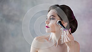 Beautiful young woman is doing herself a makeover. Girl with brush in hand to apply powder on face