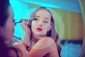 A beautiful young woman is doing herself a makeover. Girl with cerly hair doing evening makeup using brush and eyeshadow i