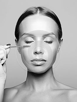 Beautiful young woman doing make-up. Black and white portrait