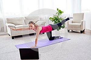 Beautiful young woman doing stretching exercise on floor at home, online training on laptop computer, copy space.