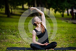 Beautiful young woman doing stretching exercise on green grass at park. Yoga workout