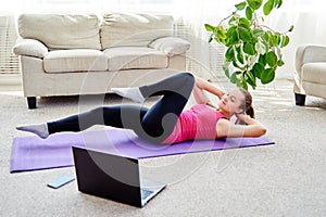 Beautiful young woman doing working out exercise on floor at home, online training on laptop computer, copy space.