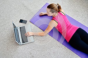 Beautiful young woman doing working out exercise on floor at home and using laptop, online training, copy space.