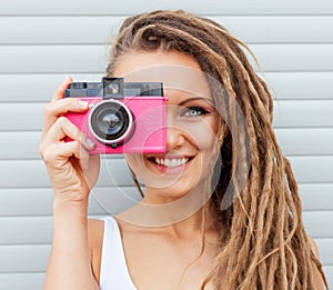 Beautiful young woman with dreadlocks taking photos with vintage pink retro film camera