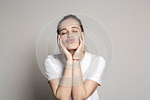 Beautiful young woman dreaming of a romantic kiss. She closed eyes, pouted lips, and laid her palms on cheeks. Funny portrait of a