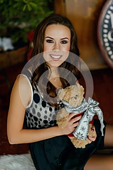 Beautiful young woman in dress in christmas interior with a teddy bear in her arms and smiling. Christmas and New Year holiday