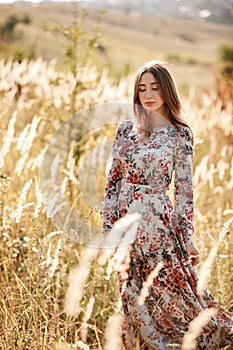 Beautiful young woman in dress in field at sunset. stylish romantic girl with long hair having fun outdoors