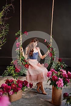 a beautiful young woman in a dress sits on a swing in peony flowers.