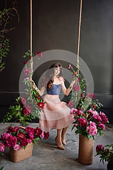 a beautiful young woman in a dress sits on a swing in peony flowers.