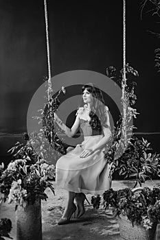 a beautiful young woman in a dress sits on a swing in peony flowers.