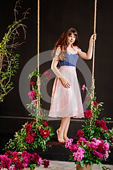 a beautiful young woman in a dress stands on a swing in peony flowers.
