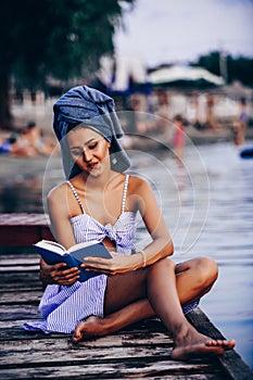 Beautiful young woman sitting on the beach enjoying while reading a book