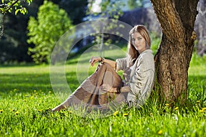 Beautiful young woman dressed in boho style sitting on green grass