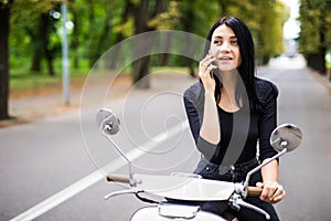 Beautiful young woman dressed casual sitting on scooter and talking on phone.