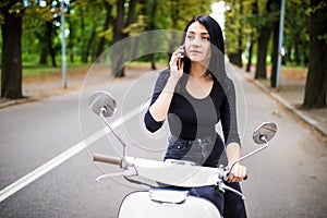 Beautiful young woman dressed casual sitting on scooter and talking on phone.