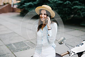 Beautiful young woman dressed casual sitting on scooter and talking on phone. Girl sitting on the bike and using Cellular smartpho