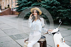 Beautiful young woman dressed casual sitting on scooter and talking on phone. Girl sitting on the bike and using Cellular smartpho