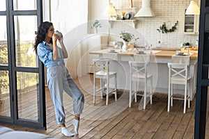 Beautiful young woman drinking coffee from cup, relaxing with hot drink at home, empty space