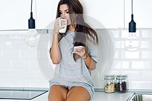 Beautiful young woman drinking coffee and using her mobile phone