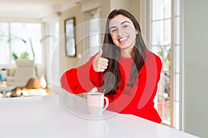 Beautiful young woman drinking a cup of black coffee doing happy thumbs up gesture with hand