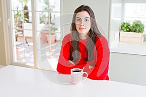 Beautiful young woman drinking a cup of black coffee with serious expression on face