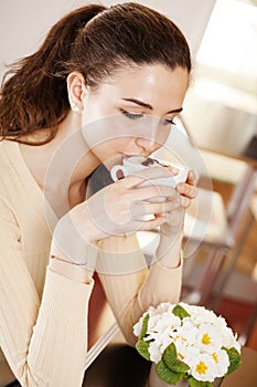 Beautiful young woman drinking a cup of coffee in her hands at the cafe coffee bar, ice cream shop and pastry shop. Portrait of