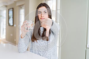 Beautiful young woman drinking a fresh glass of water with angry face, negative sign showing dislike with thumbs down, rejection