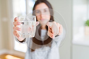 Beautiful young woman drinking a fresh glass of water pointing with finger to the camera and to you, hand sign, positive and