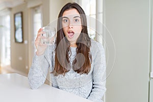 Beautiful young woman drinking a fresh glass of water scared in shock with a surprise face, afraid and excited with fear