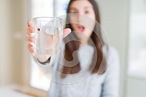 Beautiful young woman drinking a fresh glass of water scared in shock with a surprise face, afraid and excited with fear