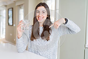 Beautiful young woman drinking a fresh glass of water with surprise face pointing finger to himself