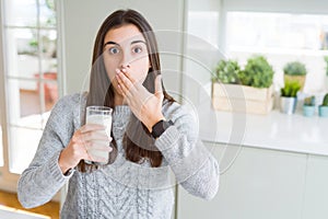 Beautiful young woman drinking a glass of fresh milk cover mouth with hand shocked with shame for mistake, expression of fear,