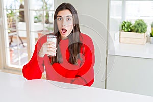 Beautiful young woman drinking a glass of fresh milk scared in shock with a surprise face, afraid and excited with fear expression