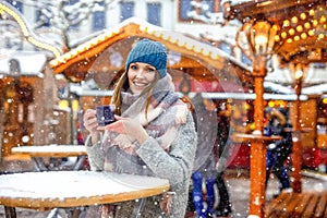 Beautiful young woman drinking hot punch, mulled wine on German Christmas market. Happy girl in winter clothes with