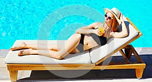 beautiful young woman drinking juice lies on deckchair over blue water pool background