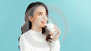 Beautiful young woman drinking milk on blue background