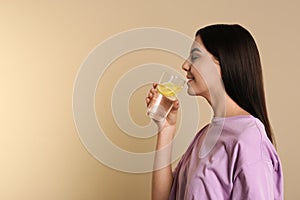 Beautiful young woman drinking tasty lemon water on beige background. Space for text