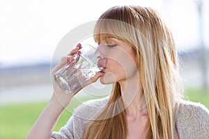 Beautiful young woman drinking water glass in the park.