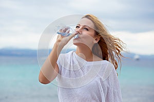 Beautiful young woman drinking water in summer beach outdoor with sea background