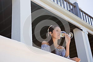 Beautiful young woman drinking white wine in balcony at restaurant