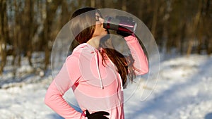 Beautiful young woman drinks tea after jogging in the winter forest.