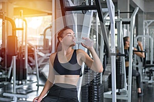 Beautiful young woman drinks water in gym. Sports nutrition concept