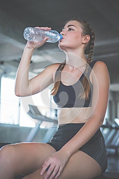 Beautiful young woman drinks water in gym. Sports nutrition concept