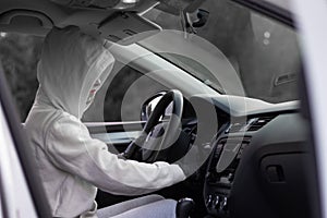 A beautiful young woman driver in a white jacket with a hood and black gloves sits at the wheel of a car. Selective focus. Portrai