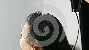 Beautiful young woman is drying her long black hair with a hairdryer in beauty salon or hairdresser