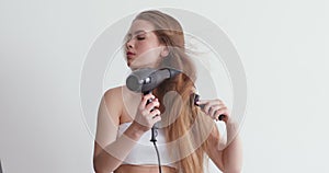 Beautiful young woman drying long hair with dryer, combing it
