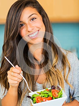 Beautiful young woman eating a bowl of healthy organic salad