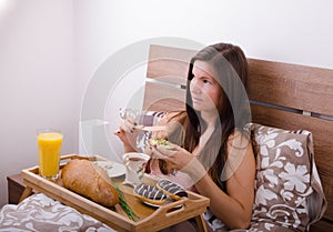 Beautiful young woman eating breakfast in bed in the morning