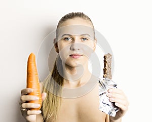 Beautiful young woman eating an carrot. carrot vs chocolate. healthy food - strong teeth concept