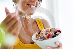 Beautiful young woman eating cereals and fruits at home.